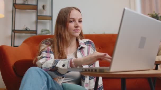Молода дівчина використовує ноутбук комп'ютер, що сидить на підлозі, інтернет-магазини з домашнього офісу — стокове відео