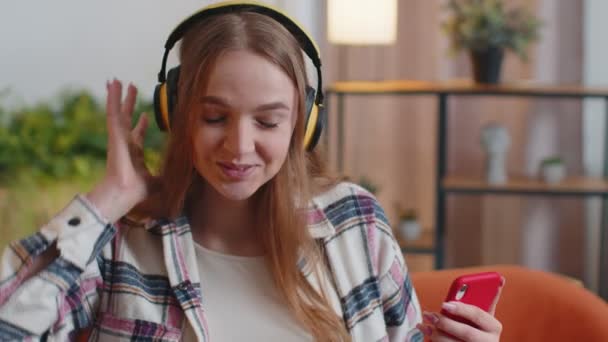 Mooie blanke jonge vrouw in koptelefoon luisteren muziek dansen, zingen in de woonkamer thuis — Stockvideo