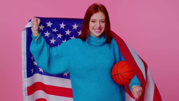 Pelirroja joven fanática del baloncesto sosteniendo bandera estadounidense haciendo gesto ganador, bailando sola — Vídeos de Stock