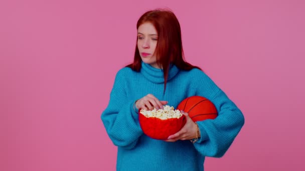 Kızıl saçlı genç bayan basketbol fanatiği patlamış mısır yiyor kazanan hareketi yapıyor, zaferi kutluyor. — Stok video