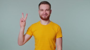 Yakışıklı, şık gülümseyen adam zafer işareti gösteriyor, başarı ve kazanmayı umuyor, barış jesti yapıyor.