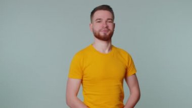 Sakallı adam kameraya dostça gülümsüyor ve el sallıyor.