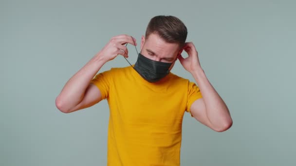 Грустный несчастный человек надевает маску на лицо, чтобы предотвратить респираторную коронавирусную инфекцию гриппа — стоковое видео
