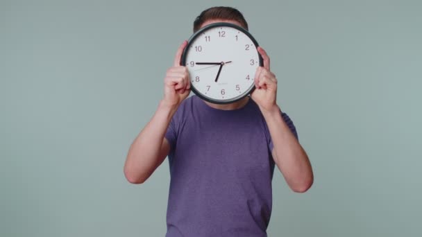 Młody człowiek trzyma zegarek, chowa się, sprawdza czas na zegarze, spóźnia się do pracy. — Wideo stockowe