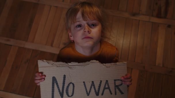 Rädd hemlös liten flicka sitter med inskription inget krig, gömmer sig från bombangrepp hemma — Stockvideo
