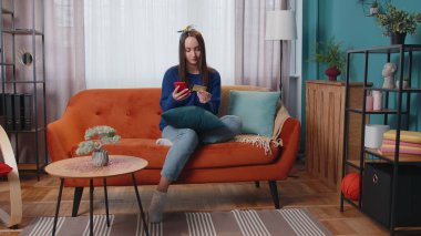 Kadın evde kredi kartı ve akıllı telefon kullanarak para transferi yapıyor.