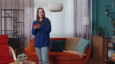 Evde duran neşeli genç kadın sosyal medya uygulamasında cep telefonu paylaşımı mesajları kullanıyor