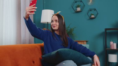 Kanepede oturan akıllı telefonlu bir kadın cep telefonu kamerasıyla selfie çekiyor. İnternetten sanal video görüşmesi.
