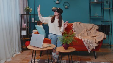 Genç kız evde sanal gerçeklik kulaklığı kullanıyor. 3 boyutlu video oyunu oynuyor. Ellerle jestler yapıyor.