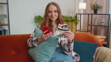 Kadın evde kredi kartı ve akıllı telefon kullanarak para transferi yapıyor.