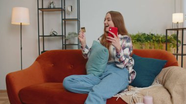 Kadın evde kredi kartı ve akıllı telefon kullanarak para transferi yapıyor.