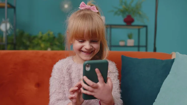 Niño niño sostiene teléfono inteligente viendo dibujos animados divertidos, charlando con amigos en el sofá solo en casa —  Fotos de Stock