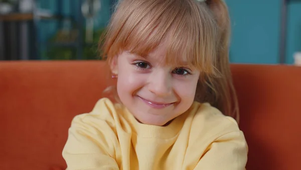 Portré kis aranyos gyermek lány ül egyedül kanapén otthon nézi a kamerát, és mosolyog — Stock Fotó