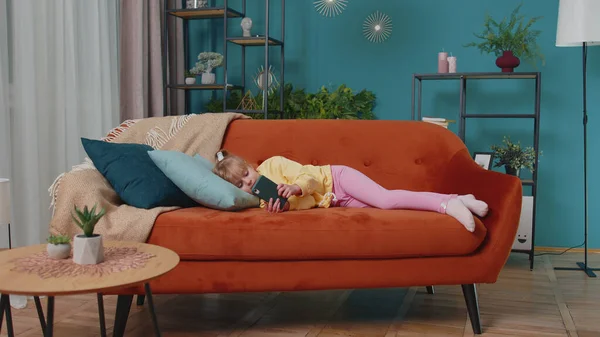 Niño niño sostiene teléfono inteligente viendo dibujos animados en línea, charlando con amigos en el sofá solo en casa — Foto de Stock