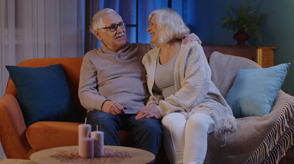Happy old senior elderly family couple hugging, laughing, smiling talking at modern home sofa
