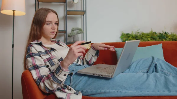 Woman sitting at home using credit bank card and laptop pc while transferring money online shopping