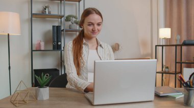 Masada oturmuş laptopunu açan beyaz bir kadın merkez ofisteki bir odada çalışmaya başlıyor.