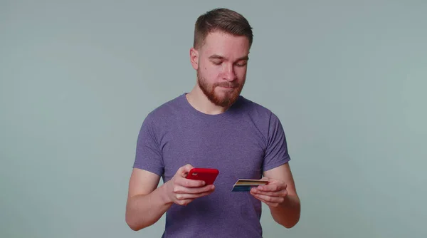 Mann nutzt Kreditkarte und Smartphone beim Geldtransfer, kauft online ein — Stockfoto