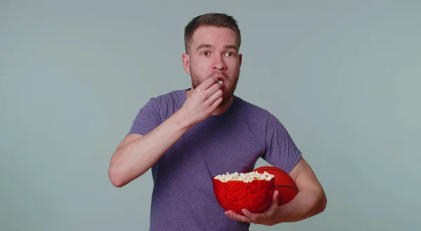 Barbuto giovane fan di basket mangiare popcorn facendo gesto vincitore, celebrando la vittoria — Foto Stock