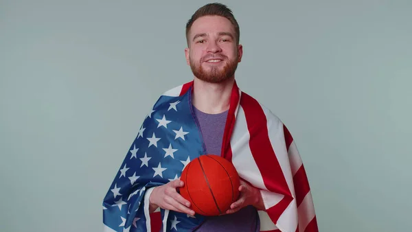 Ventilador de basquete barbudo jovem segurando bandeira americana dos EUA fazendo gesto vencedor, dançando sozinho — Fotografia de Stock