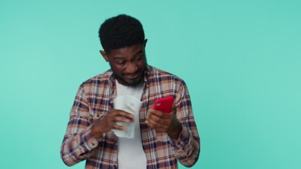 Glad afrikansk amerikansk man mobiltelefon display uppriktigt glädjande vinna, ta emot pengar dollar kontanter — Stockvideo