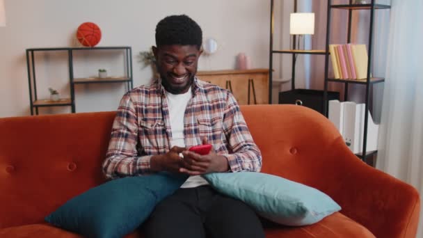 Fiatal felnőtt férfi otthon használja mobiltelefon gépelés böngészés mondani wow igen kiderült, nagy győzelem — Stock videók