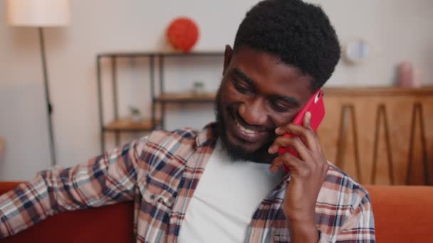 Ung vuxen afrikansk amerikansk man njuter prata mobiltelefon samtal med vänner hemma — Stockvideo