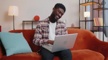 Afro-Amerikalı genç adam oturma odasında bilgisayarını kapatıp bilgisayarını kapatıyor.