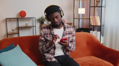 Kulaklıklı Afro-Amerikalı genç adam müzik dinliyor, dans ediyor, evde şarkı söylüyor.