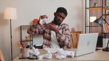 Ofiste çalışan üzgün genç adam, kötü fikirleri ve hataları olan kağıt yığınlarını dağıtıyor.