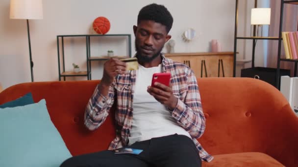 Чоловік сидить вдома за допомогою кредитної банківської картки та смартфона під час переказу грошей онлайн покупки — стокове відео
