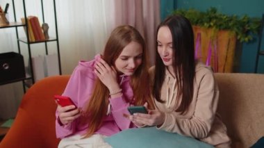 Heyecanlı kız arkadaşlar kardeşler evdeki kanepede akıllı telefondan fotoğraf izleyip sosyal medyanın tadını çıkarıyorlar.