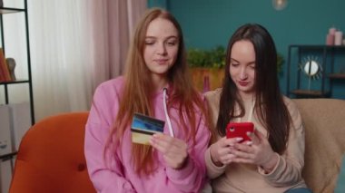 Neşeli kızlar kredi kartı ve akıllı telefon kullanarak para transferi ve alım yapıyor.