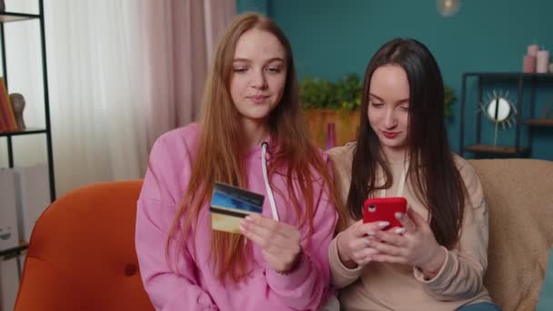 Neşeli kızlar kredi kartı ve akıllı telefon kullanarak para transferi ve alım yapıyor. — Stok video