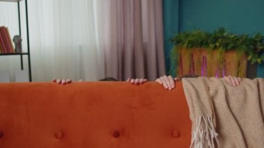 Kurnaz kız arkadaşlar saklambaç oynayan kardeşler kanepenin yanında kamera karşısında oyun oynuyorlar.