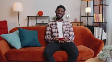 Mutlu genç adam koltukta oturuyor, cep telefonu paylaşımı mesajı kullanıyor.