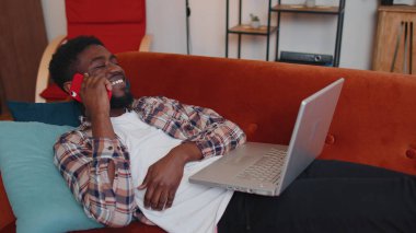 Dizüstü bilgisayar kullanan genç adam kanepede oturuyor, çalışıyor, internetten alışveriş yapıyor.