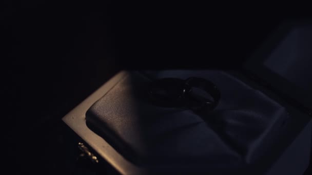 İki altın evlilik yüzüğü beyaz hediye kutusunun üzerinde duruyor. Ilık ışıkla parıldıyor. Makroyu kapat. — Stok video