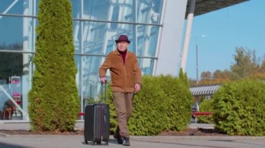 Emekli kıdemli turist büyükbaba işadamı havaalanı kapısından bavul çantasıyla geliyor.