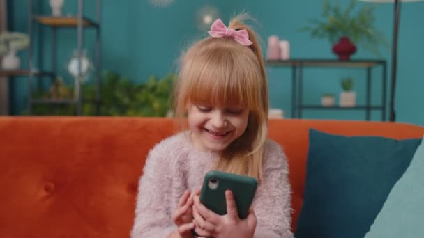 Criança criança segurar smartphone assistindo desenhos animados engraçados, conversando com amigos no sofá sozinho em casa — Vídeo de Stock