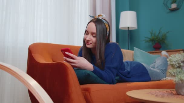 Young caucasian woman lying on couch using smartphone watching video, online shopping, tapping — Stock Video