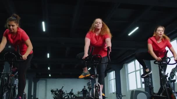Healthy Caucasian group of women exercising workout on stationary cycling machine bike in gym — Stockvideo