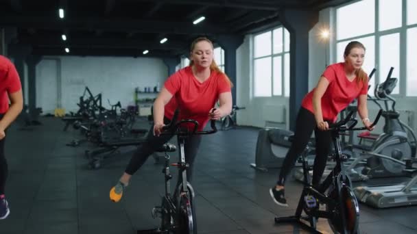 Group athletic girls performing aerobic riding training exercises on cycling stationary bike in gym — Stockvideo
