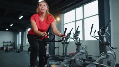 Spor salonunda bisiklete binen atletik genç bir kadın spor salonunda spor yapıyor, evde kilo kaybediyor.
