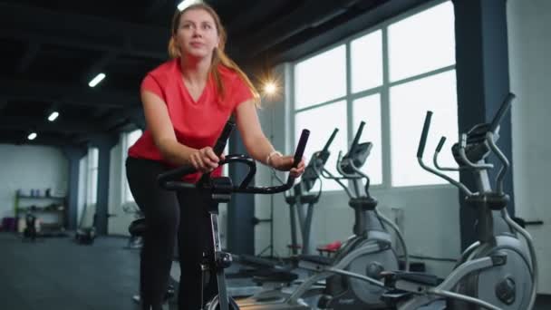 Athletic young woman riding on spinning stationary bike training routine in gym, weight loss indoors — Stockvideo