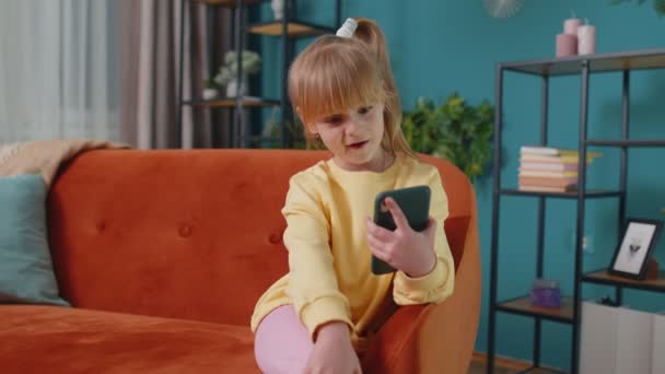 Ragazza bambino godendo conversazione sul telefono cellulare con un amico rilassante seduto sul divano a casa da solo — Video Stock