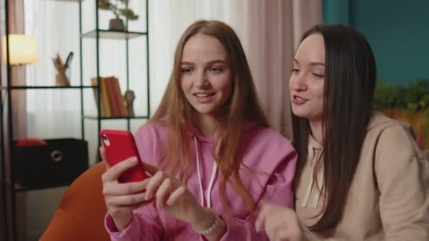 Χαρούμενα κορίτσια φίλους αδέλφια βλέποντας φωτογραφίες στο smartphone στον καναπέ στο σπίτι, να απολαύσετε τα μέσα κοινωνικής δικτύωσης — Αρχείο Βίντεο