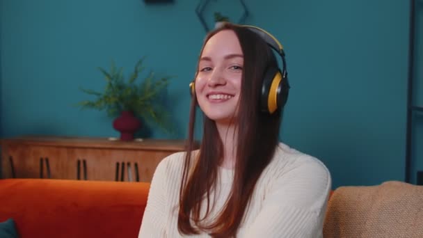 Radostná mladá žena v bezdrátových sluchátkách tančí, zpívá na útulném gauči v obývacím pokoji doma — Stock video