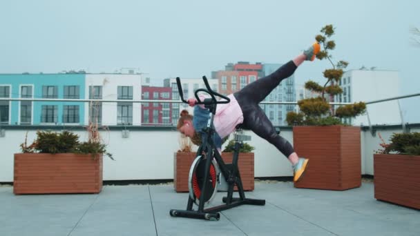 Αθλητική γυναίκα κάνει σπάγκο προπόνηση ρουτίνας για την περιστροφή στατικό ποδήλατο στην οροφή του σπιτιού, απώλεια βάρους — Αρχείο Βίντεο