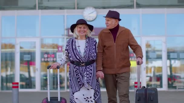 Nyugdíjas turisták nagypapa sétál a reptéri csarnokból csomagokkal a kerekeken — Stock videók